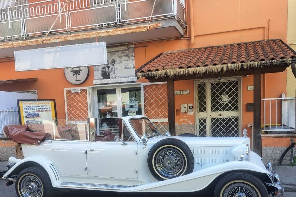 La vetrina con l'insegna L'Auto Sposa, con un'auto scoperta bianca dagli interni scuri parcheggiata davanti